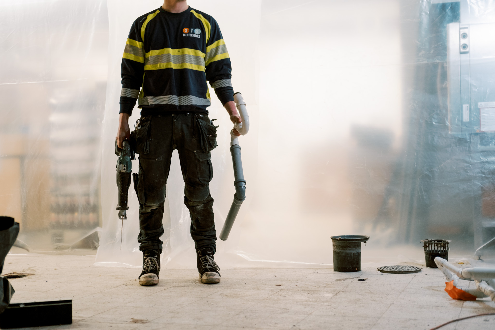 Lvi-ammattilainen kantaa viemäriputkea ja sähkötyökaluja.